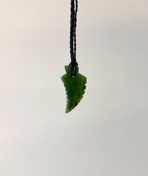 Green jade leaf-shaped pendant on a black cord against a light gray background